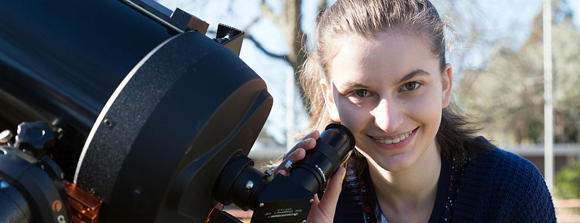 Female student smiles while using large telescope