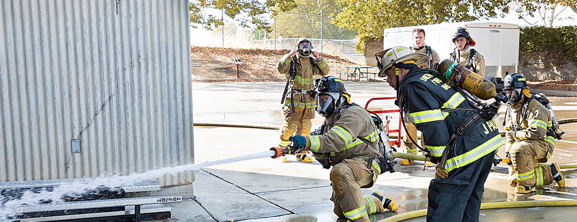 Firefighting student practices using fire hose as instructor and students observe