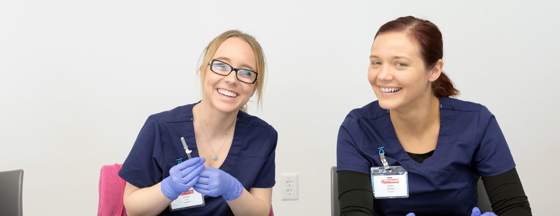 Two smiling female phlebotomy students wearing scrubs