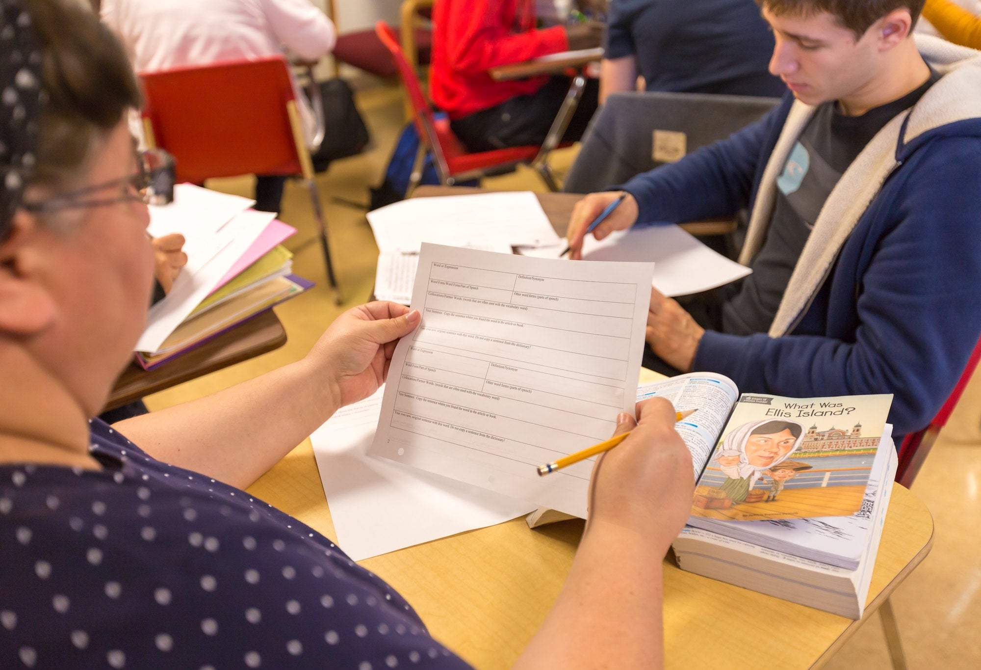 Student preparing to fill out questionnaire in class with book on desk.