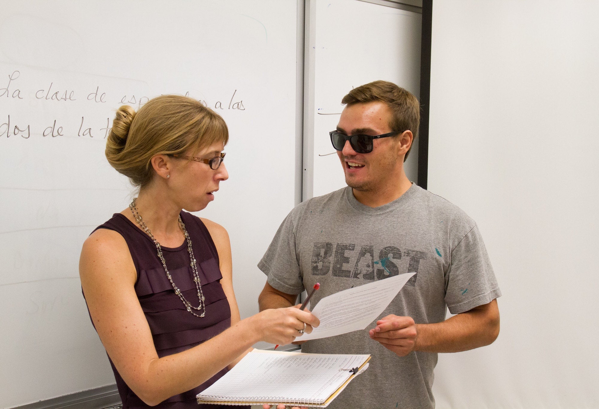 Student With Professor in front of whiteboard with spanish writing speaking about assignment.