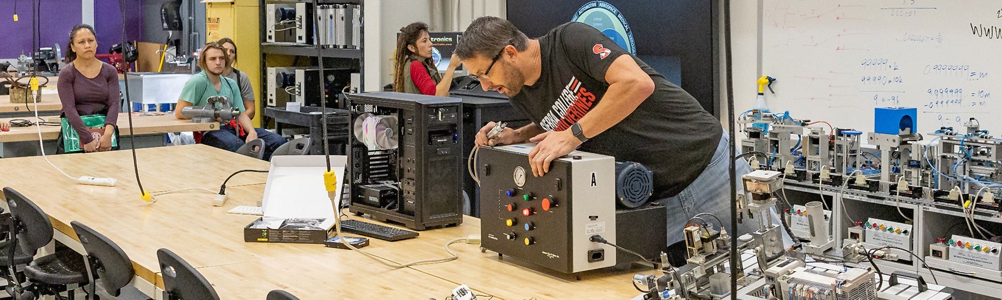 Mechatronics instructor working on product as students look on