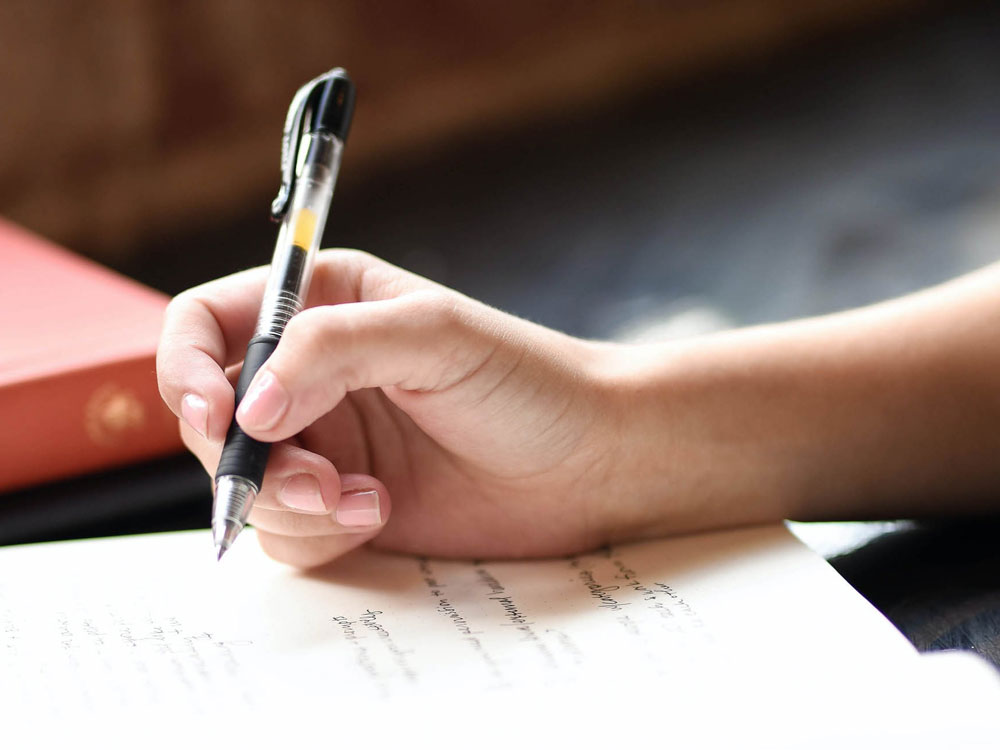 A person's hand holding a pen and writing on the paper