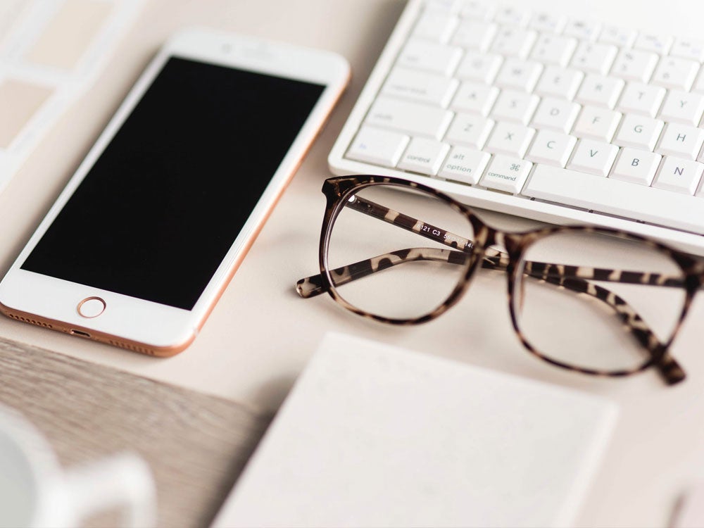Iphone and glasses on the desk next to the computer keyboard