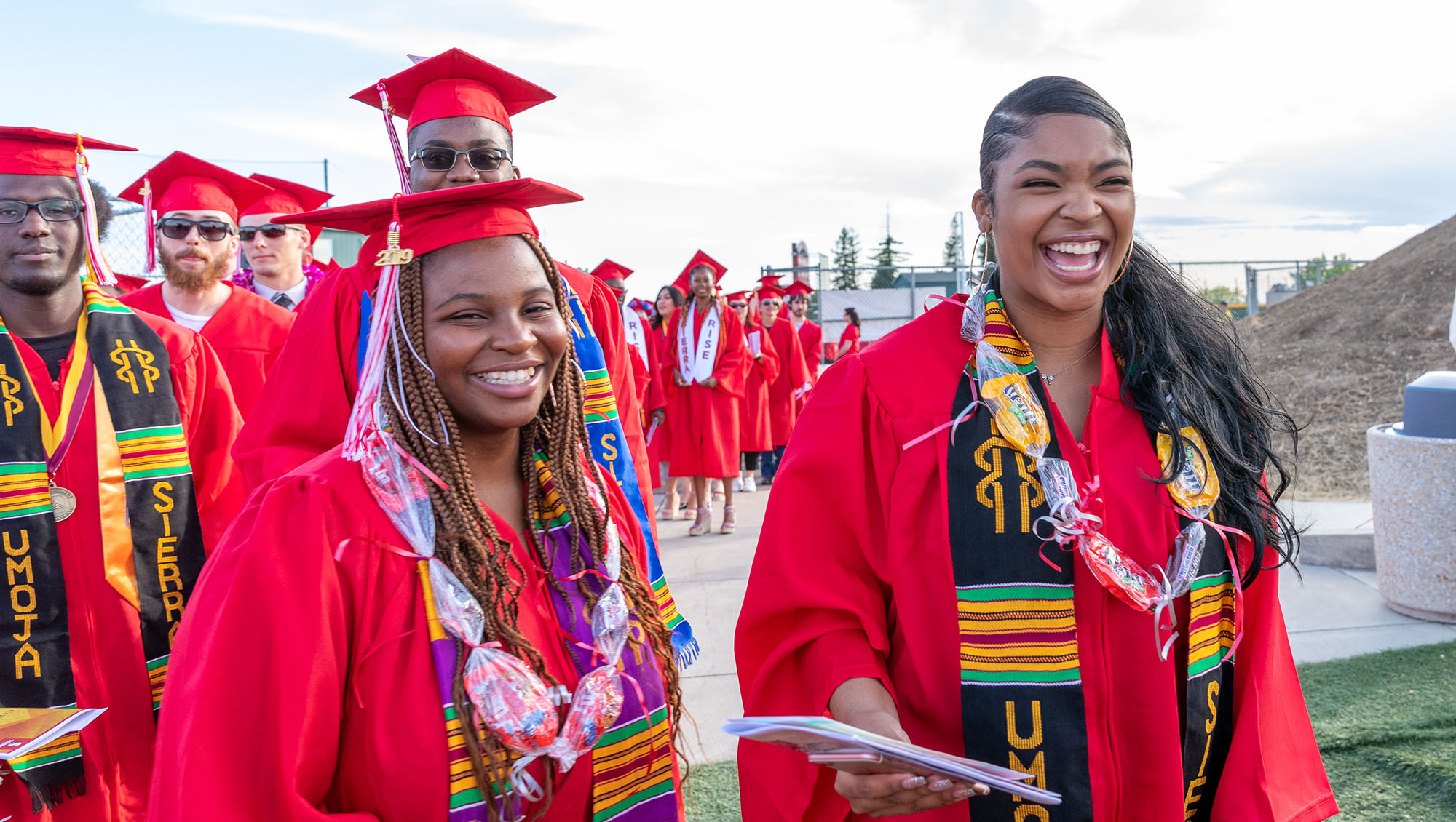 Four smiling Sierra College graduates dressed in graduation attire and Umoja stoles