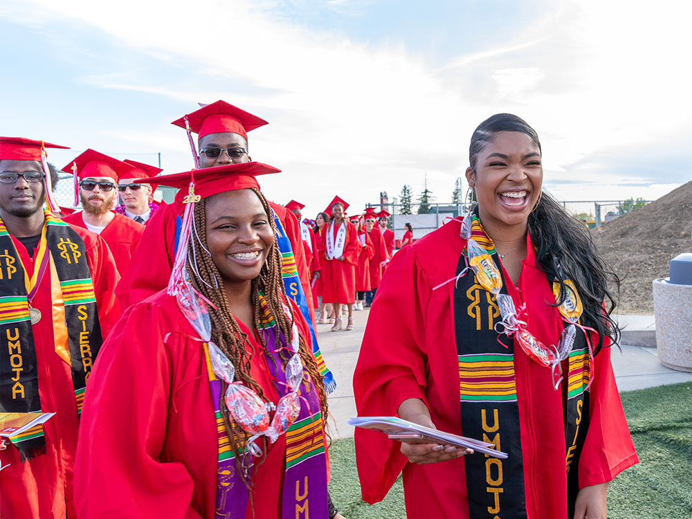Four smiling Sierra College graduates dressed in graduation attire and Umoja stoles