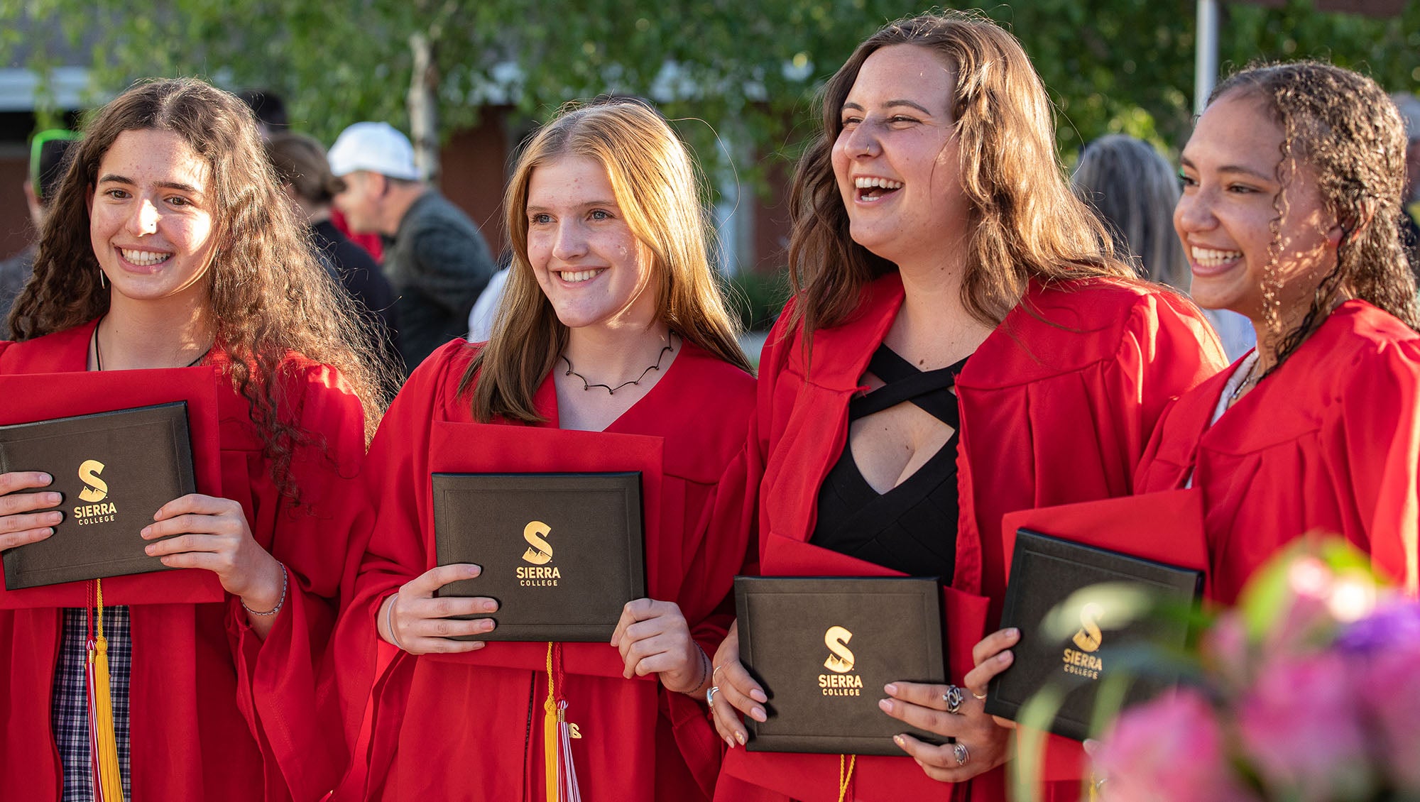 Four female students wearing graduation robes and holding diplomas