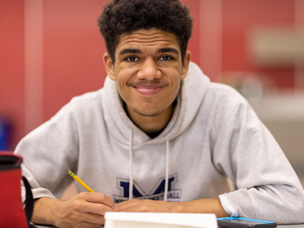 Student smiling at camera while doing homework