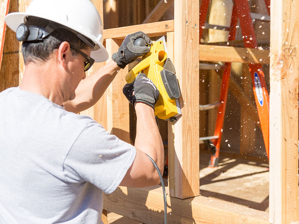 Man wearing safety gear while using an electric sander to smooth down the column of a new building structure.