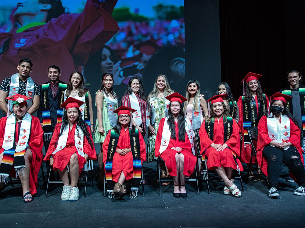 Group of male and female scholarship recipients wearing red graduation caps and gowns.