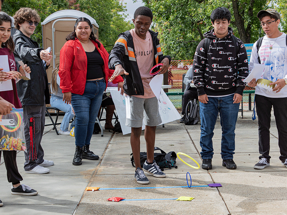 Students gather to watch a student play ring toss game
