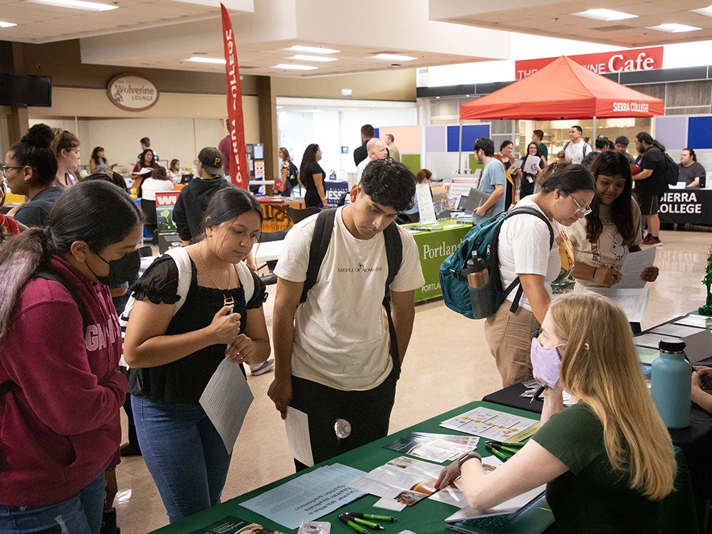 Five students review college print materials while talking to a college representative.