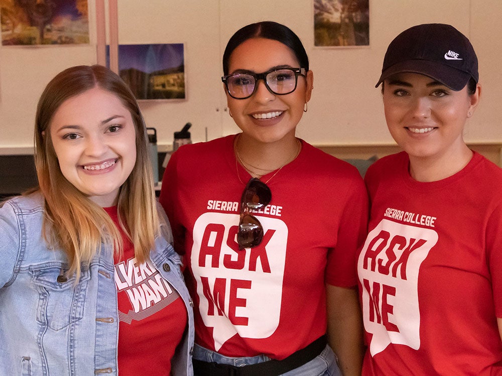 Three Sierra College staff women wearing red Ask Me and Wolverines Wanted shirts at Welcome Event on Rocklin campus.