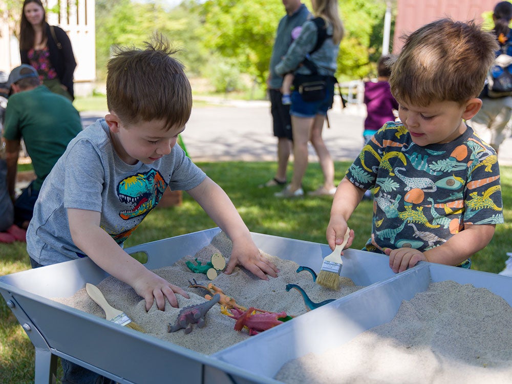 Two young boys dig in sand to find dinosaurs