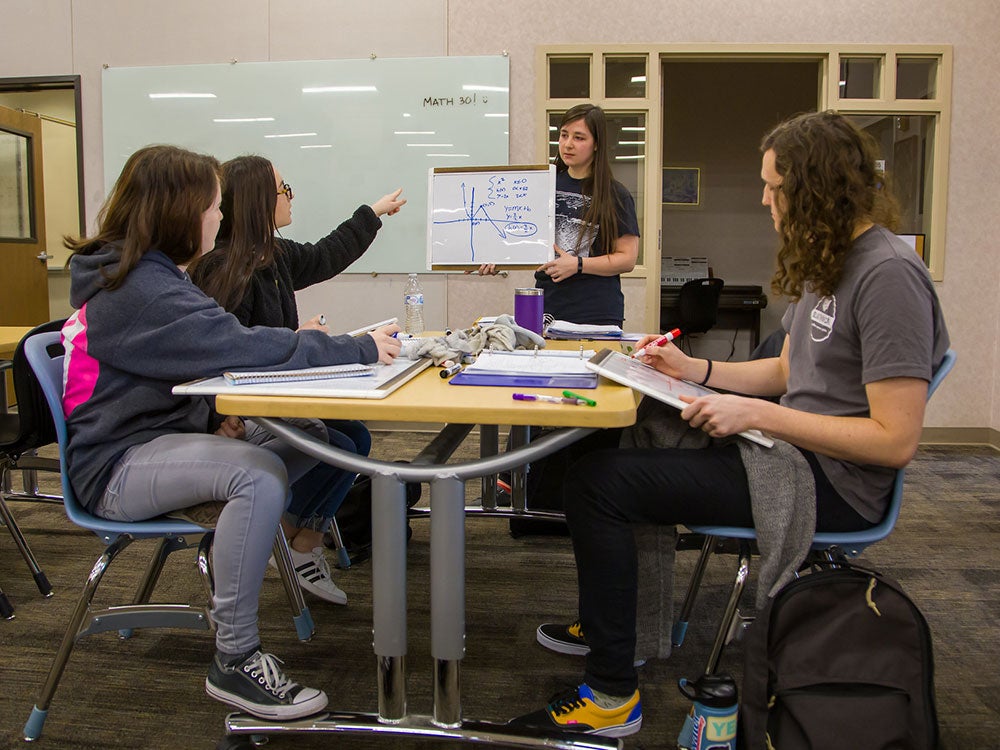 Student tutor showing three students how to solve math problem on white board in NCC Learning Center