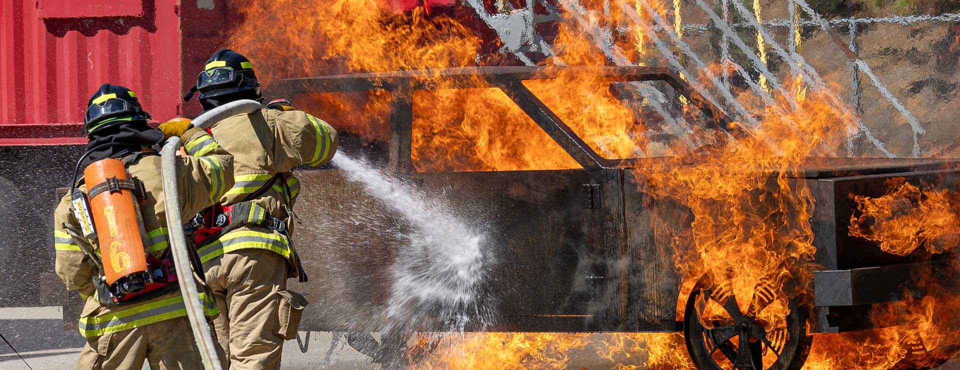 Two students hosing car fire as instructor looks on