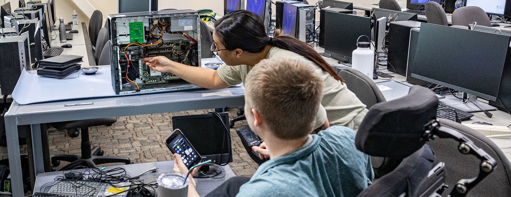 Information technology students sitting in front of classroom computers listening to IT instructor