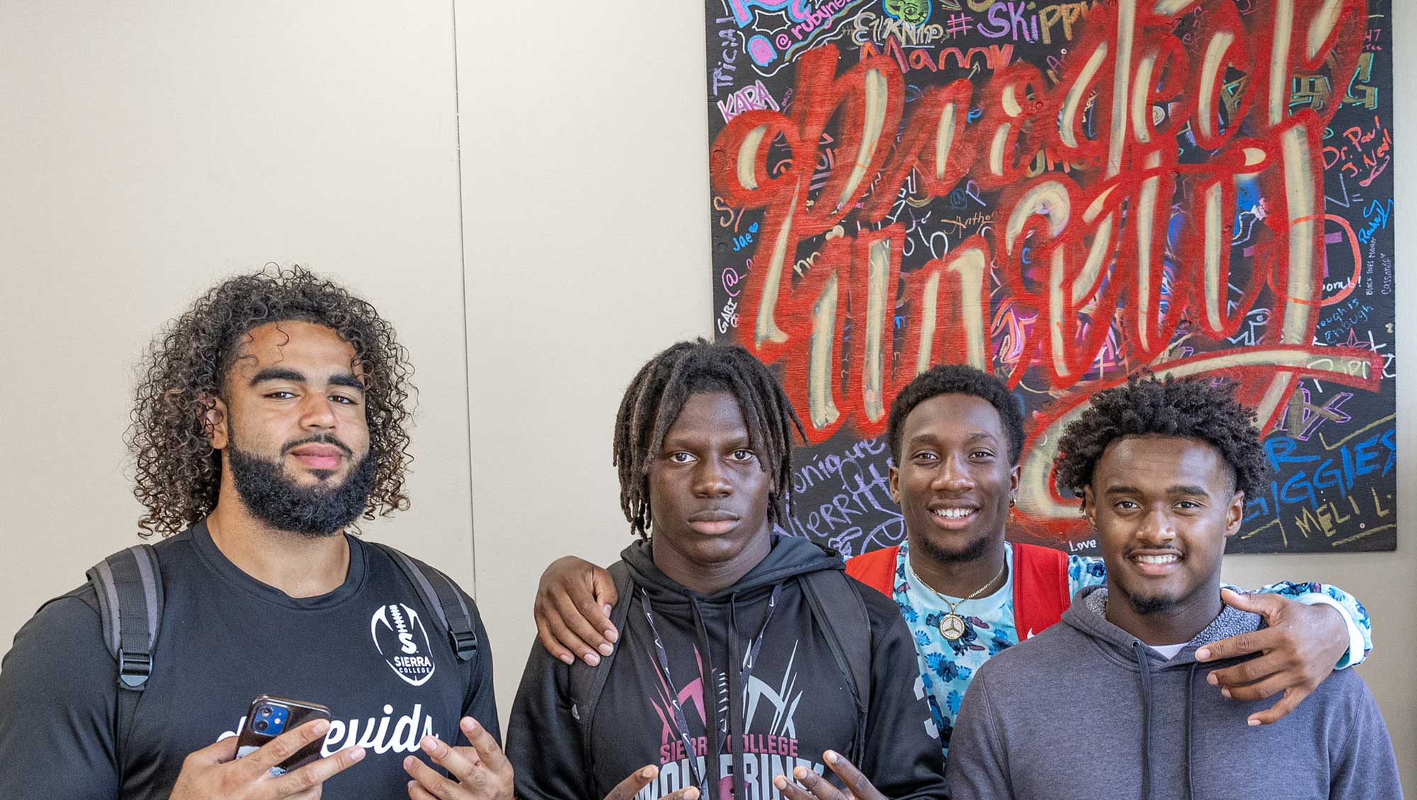 Four students in Cross Cultural Center in front of Protect Unity art