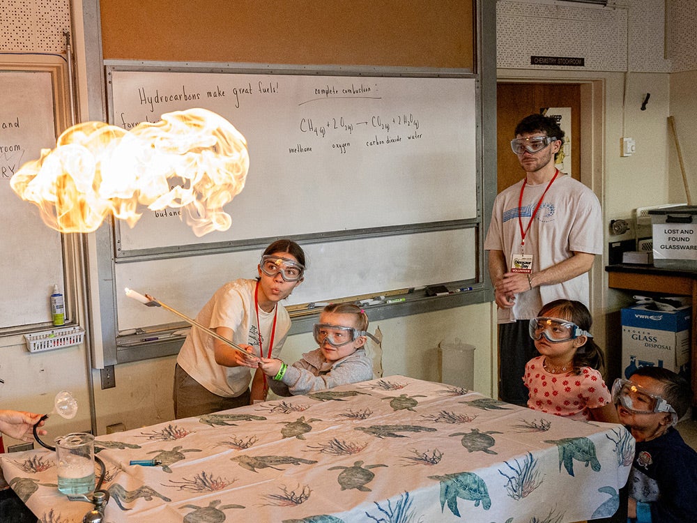 Students show three young Dino Day attendees a science experiment that makes fire.