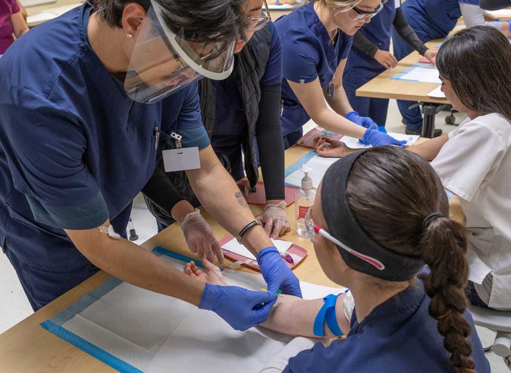 Phlebotomy instructor showing students how to take blood draw using oranges.