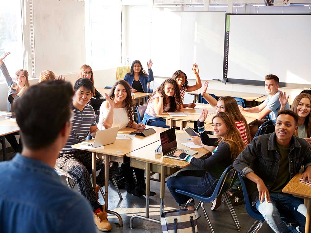 Rear View Of Male High School Teacher Standing At Front Of Class Teaching Lesson