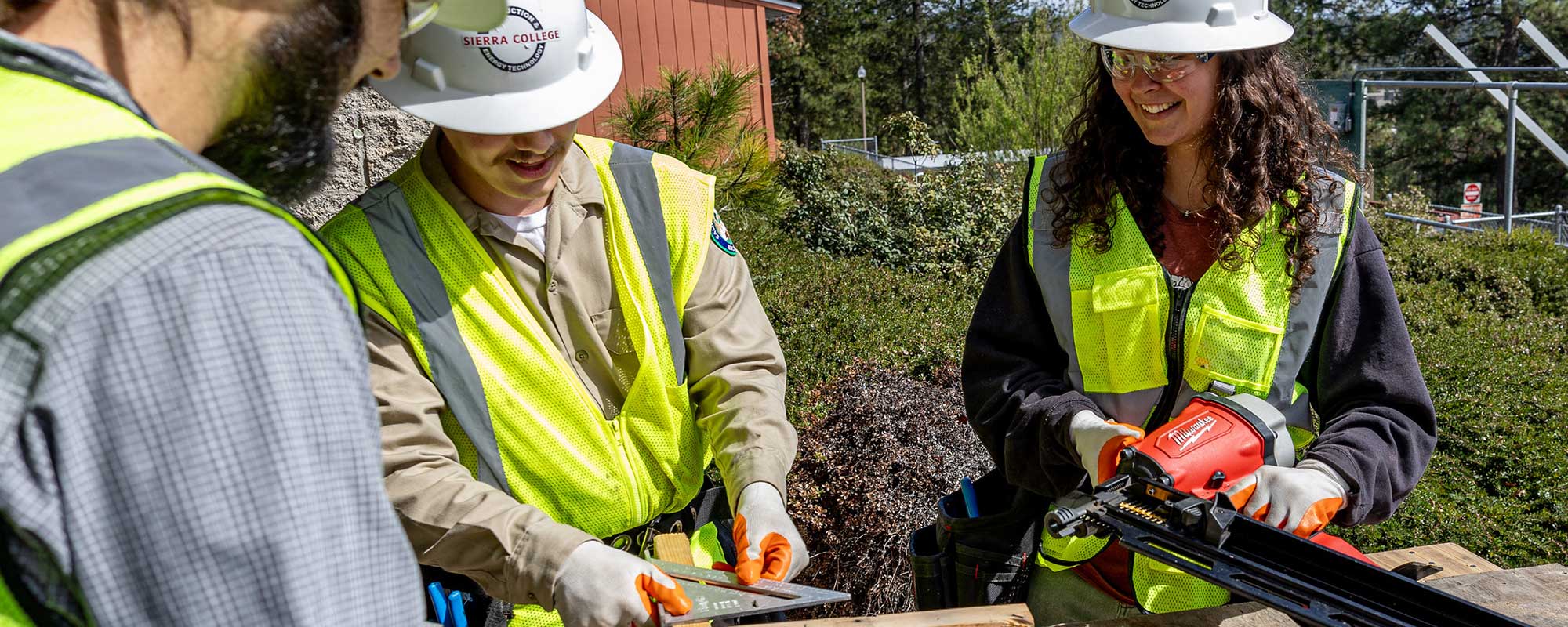 Three students use a measure and nail gun on construction project